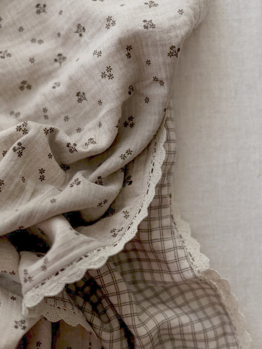 Manta de bebé em tons neutros com motivo floral de dupla face em musselina, com rendinha, ideal para aconchegar o bebé em casa ou no passeio.