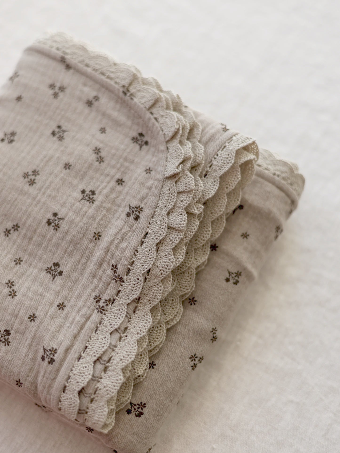 Manta de bebé em tons neutros com motivo floral de dupla face em musselina, com rendinha, ideal para aconchegar o bebé em casa ou no passeio.