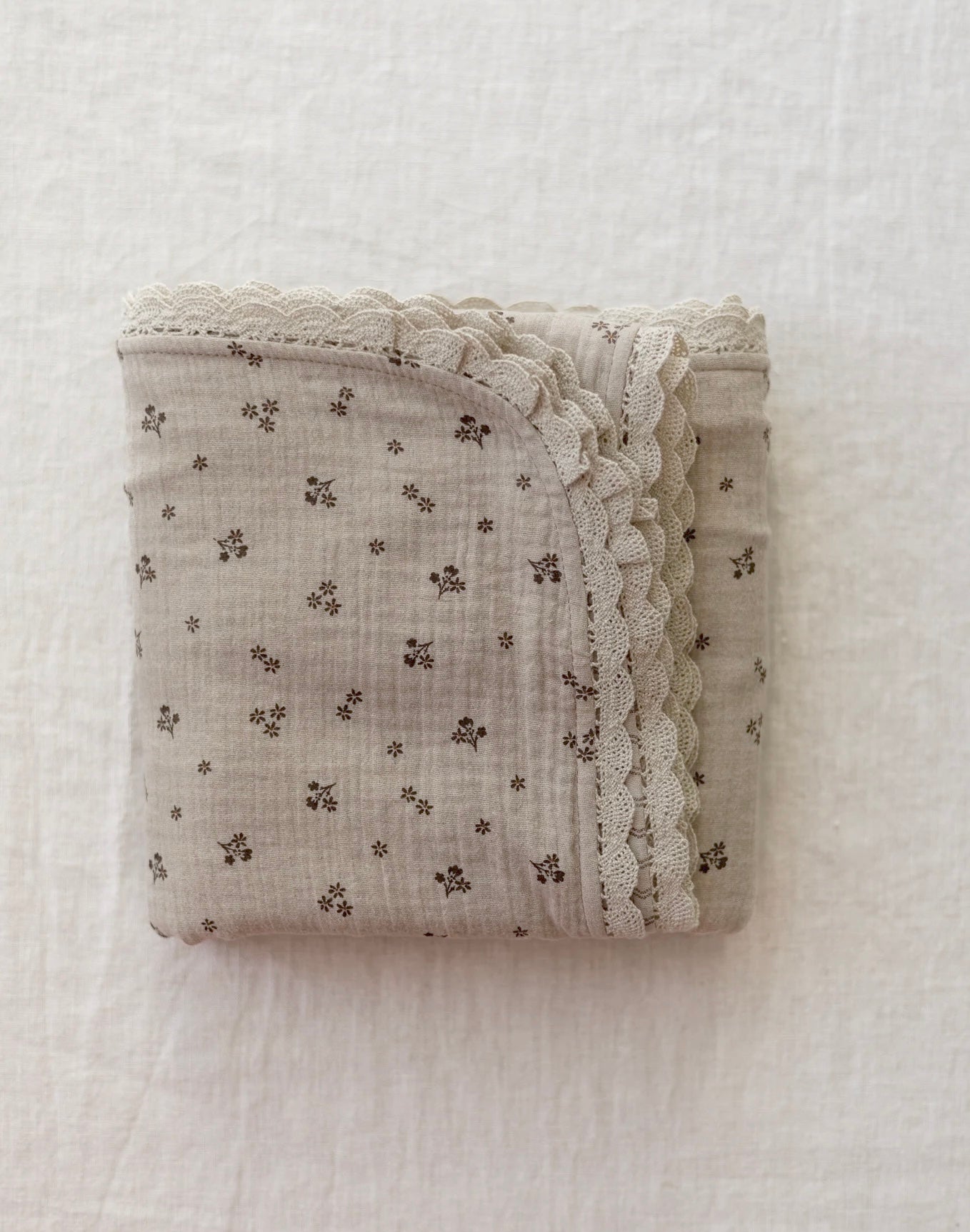 Manta de bebé em tons neutros com motivo floral de dupla face em musselina, com rendinha, ideal para aconchegar o bebé em casa ou no passeio.