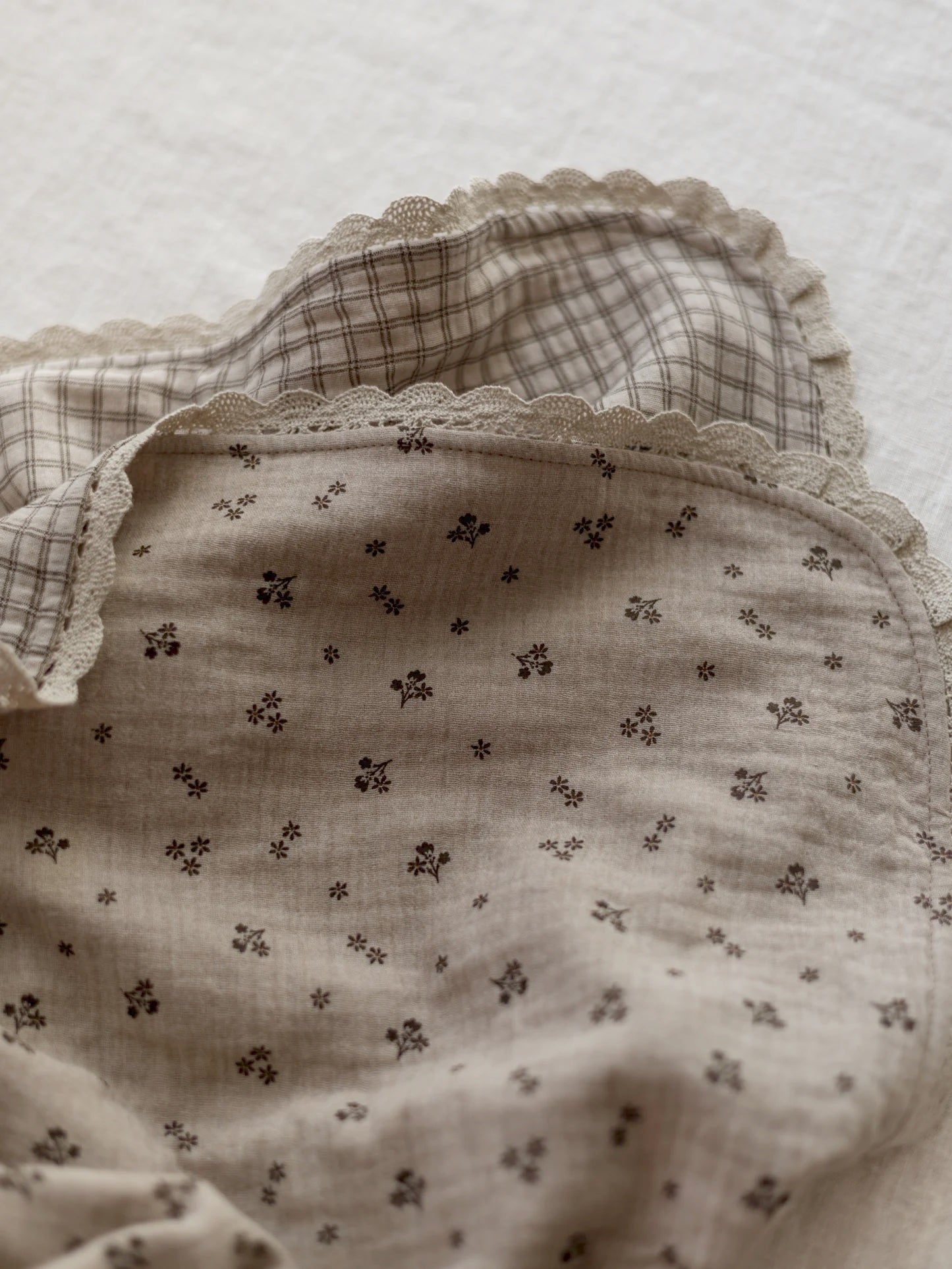 Manta de bebé em tons neutros com motivo floral de dupla face em musselina, com rendinha, ideal para aconchegar o bebé em casa ou no passeio.