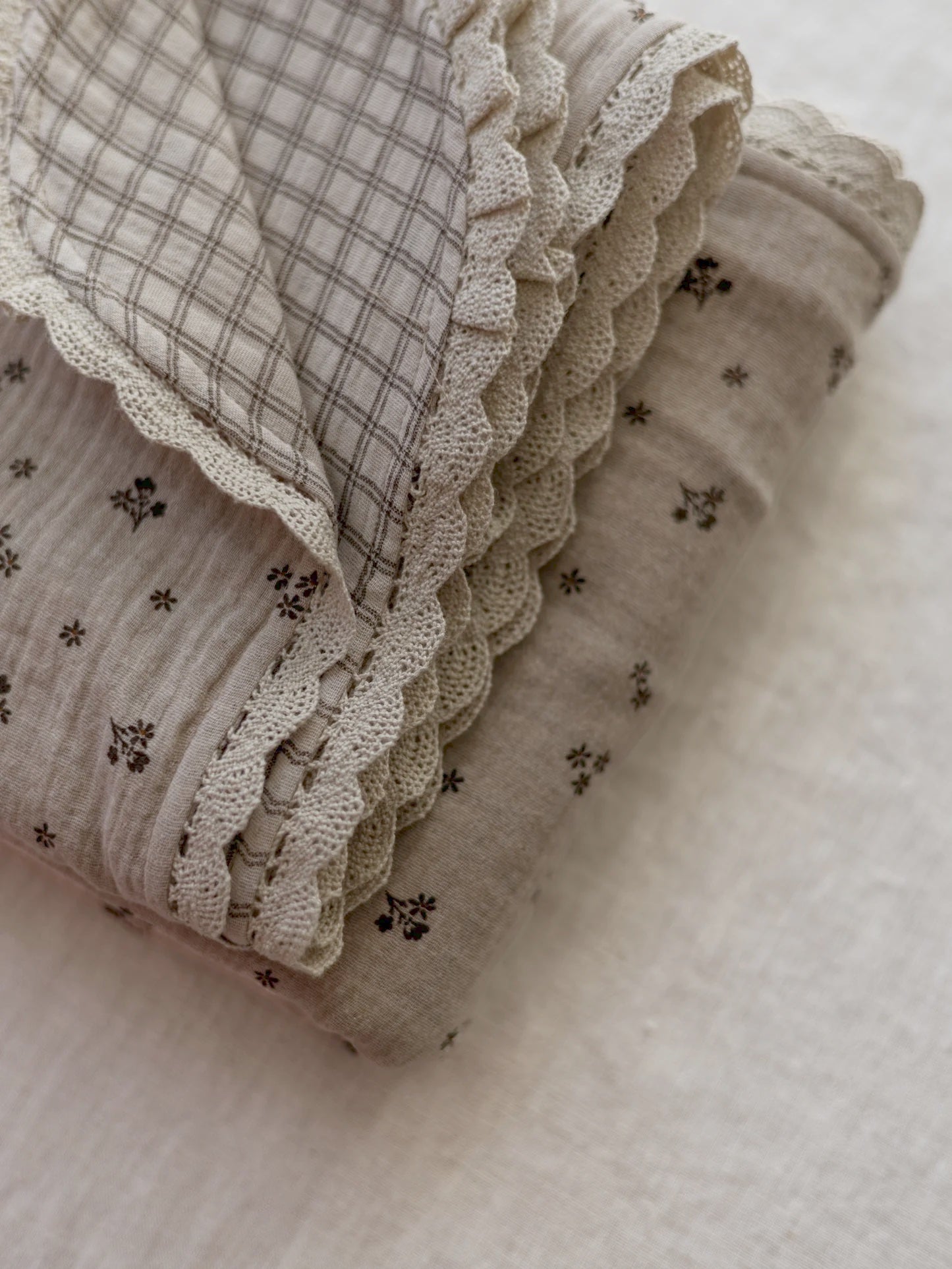 Manta de bebé em tons neutros com motivo floral de dupla face em musselina, com rendinha, ideal para aconchegar o bebé em casa ou no passeio.