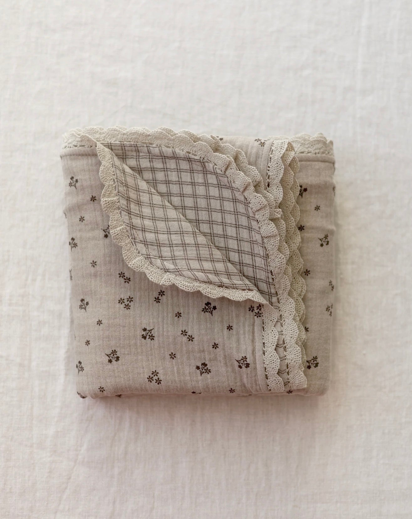Manta de bebé em tons neutros com motivo floral de dupla face em musselina, com rendinha, ideal para aconchegar o bebé em casa ou no passeio.